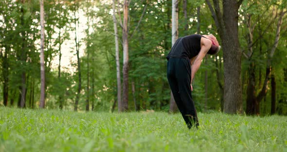 Young Men in Black Clothes Practicing Yoga and Meditating in Park at Sunny Summer Day