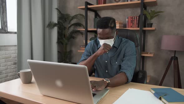 Young Black Businessman Coughs Into Protective Face Mask Working in the Office. African American Man