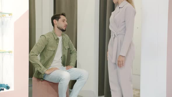 Annoyed Man Talking to Girlfriend Trying on Clothes in Fitting Room Not Happy with Shopping