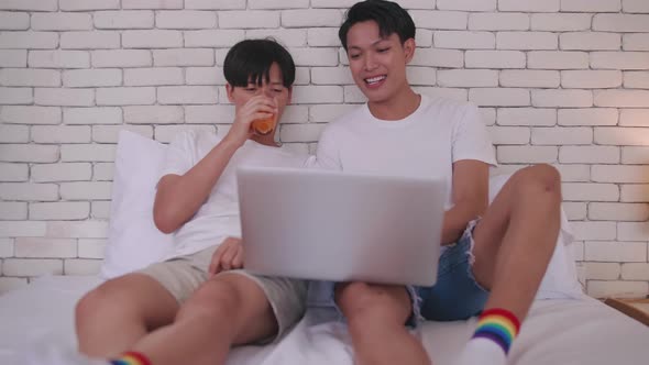 Happy gay Asian couple spending time together in bed at home.