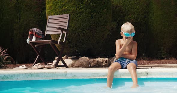 Child baby boy sitting in front of the swimming pool and dives in to blue water
