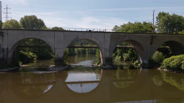 Young man standing on a footpath underneath a train bridge that reflects perfectly in the flat brown