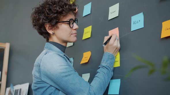 Young Woman Writing on Sticky Notes Planning Business in Modern Creative Office