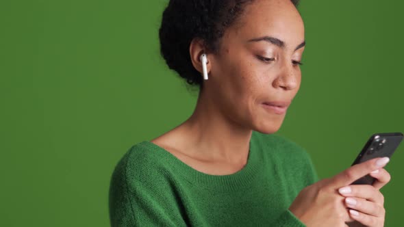 Smiling African woman in green shirt texting by phone in headphones