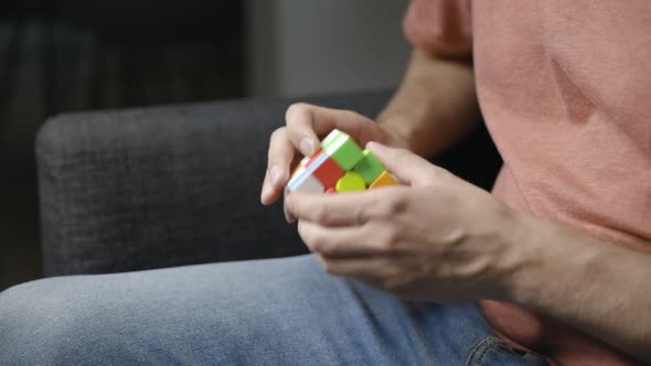 Young male hands turn and twist sides of Rubik’s cube, seen from side