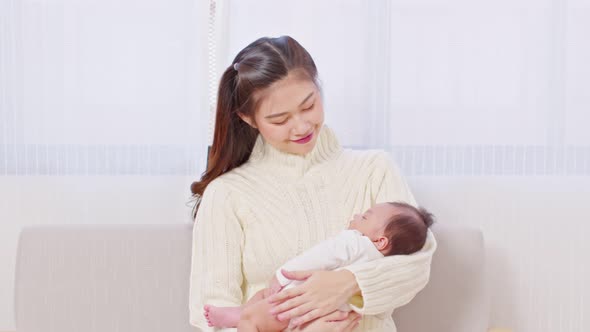 Beautiful Asian mom woman holding newborn baby in her arms sit on bed