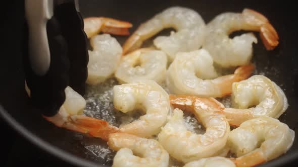 Unrecognizable cook frying prawns in pan with hot oil