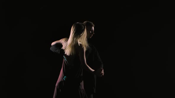 Couple of Ballroom Dancers Perform Bachata Dance Element on Black Studio Background in Darkness