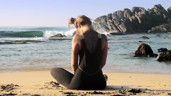 Beautiful Lady Meditates on Sandy Beach Against Ocean