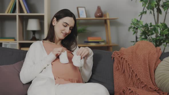 Future Mother Holding Small Baby Shoes on Belly at Home