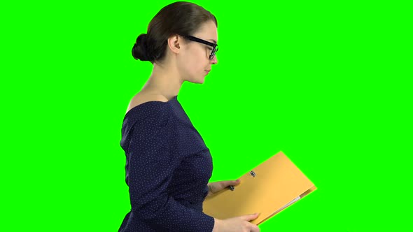 Girl Is Walking Along the Street with a Yellow Folder in Her Hands. Green Screen. Side View