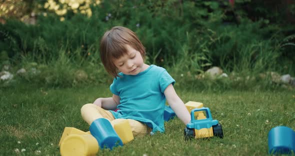 Small Cute Boy is Playing with Toy Car and Cubes on the Green Grass