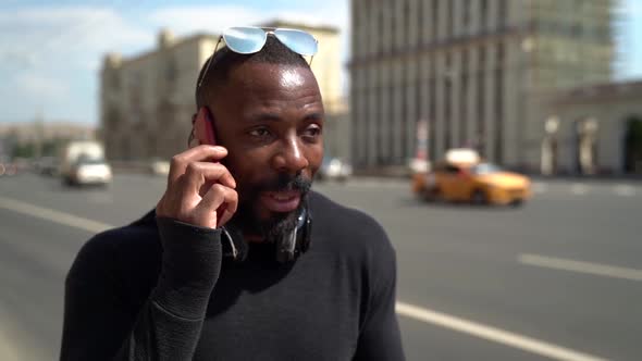 Portrait of a Serious African-American Man on a City Street on the Background of a Highway with Cars