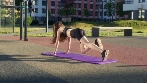 Athletic Slender Girl in Black Tight Uniform Does Plank Run on Street on Sports Ground in