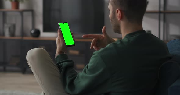 Man Is Chatting Online By Video Chat in Mobile Phone Sitting at Home on Couch in Living Room Green