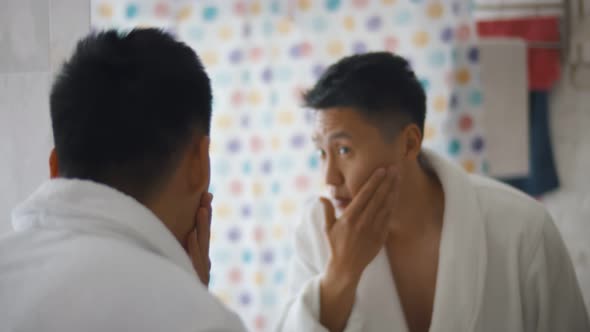 Close-up Shot of Handsome Young Asian Man Admiring Looking at His Face in Bathroom Mirror.