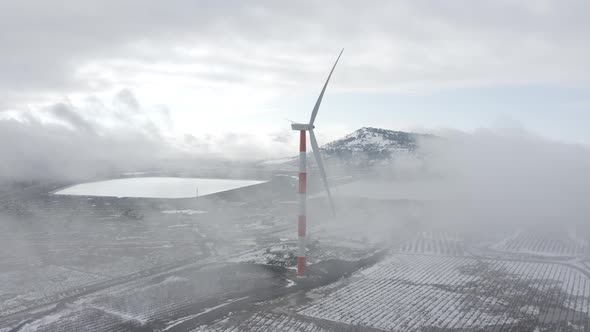 Wind turbine in a snowy landscape with early winter morning mist.