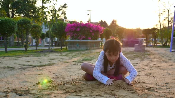 Asian Girl Playing Sand In Playground Under Sunset