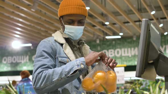 Black Man in Disposable Mask and Denim Jacket Weighs Oranges