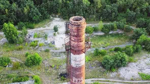 Abandoned pipe among nature. Old brick tower surrounded by green trees in summer. 