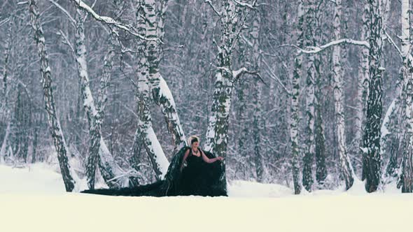 Model in Black Phoenix Suit Falls Onto Snow in Winter Forest