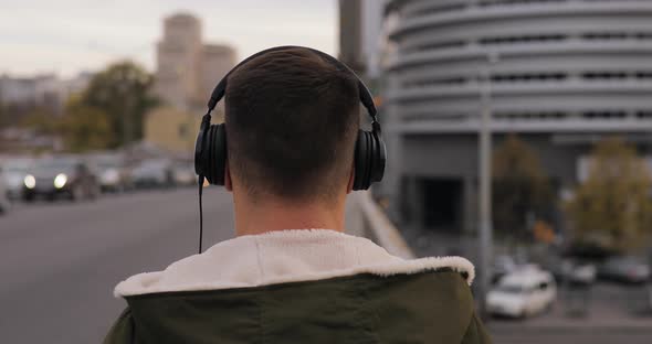 Rear View of Man Listening To Music with Headphones Walking on City Bridge