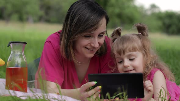 Family Weekend Picnic. Daughter Child Girl with Mother Study Lessons on Tablet. Distance Education