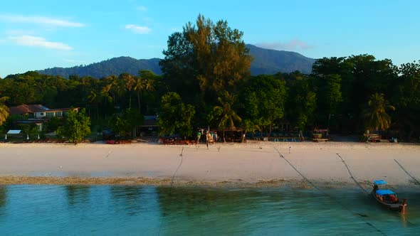 Aerial shot of a beach with white sand, boat being park, an ocean and green trees in the background.