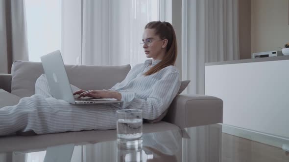 Serious Attractive Young Woman Sitting on Sofa Using Laptop Communicating Working Online at Home