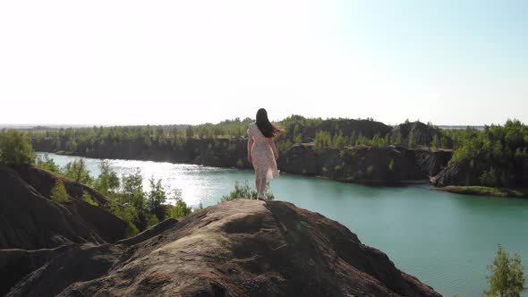 Beautiful Slender Woman in Long White Dress Approaches Edge of Abyss and Spreads Her Arms to Sides