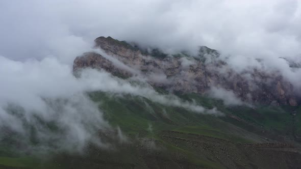 Drone Flight above green fields at the mountains in the clouds and fog.