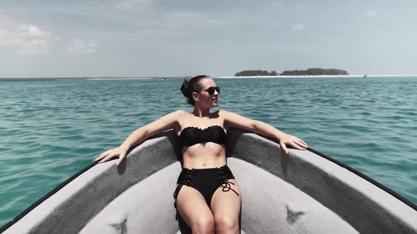 Young Woman in a Bikini and Sunglasses Lies on the Bow of Boat Floating By Ocean