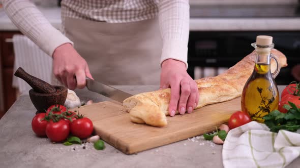 Woman Slicing Baguette on Wooden Cutting Board at Domestic Kitchen