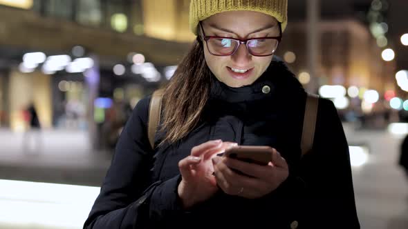 Authentic shot of woman using smart phone in the city at night in London