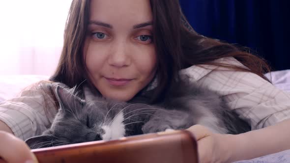 A Young Woman Lies on a Bed with a Fluffy Beautiful Cat