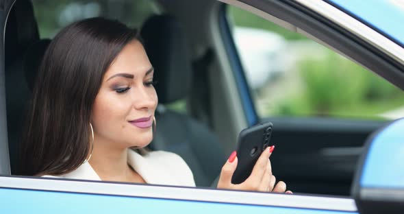 Young Woman Driver Types Messages to Friend on Phone Smiling