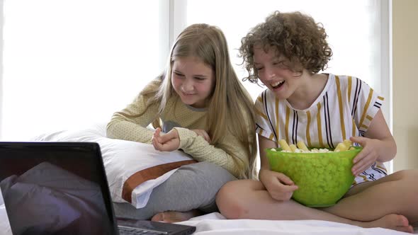 Portrait of Happy Teenage Girls Watching Comedy in Bed and Laughing. Cheerful Friends Eating Tasty