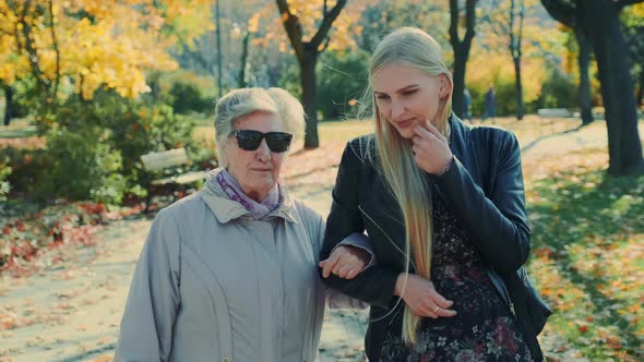 Old Woman Walking Together with Cheerful Blonde Girl in Autumn Park