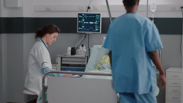 Nurse with Dark Skin Helping Patient to Sit Comfortable in Hospital Ward