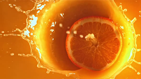 A Round Piece of Orange Falls Into the Orange Juice with Splashes