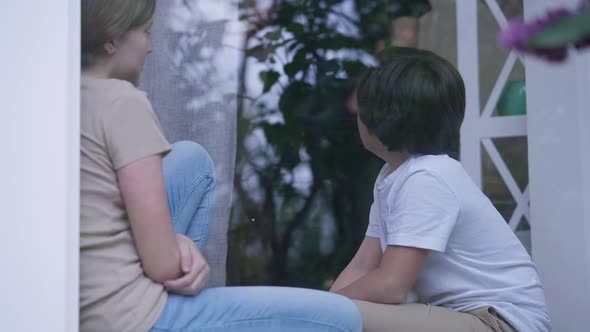 Frightened Scared Teenage Girl and Little Boy Sitting on Windowsill As Angry Violent Unrecognizable
