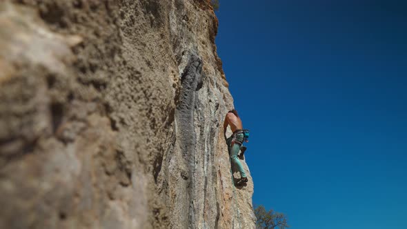 Side View of Young Strong Man Rock Climber in Bright Blue Pants Climbing on Cliff