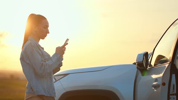 Young Woman Using on Smartphone Against Sunset Background