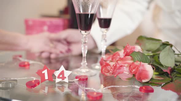 Close-up of Bouquet of Roses and Wineglasses Standing on Glass Table. Mature Male Hand Taking Senior