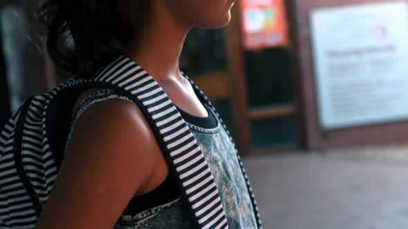 Thoughtful schoolgirl standing with schoolbag