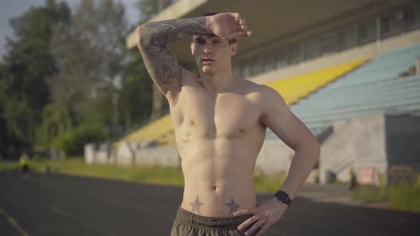 Middle Shot of Perspiring Sportsman Wiping Forehead with Tattooed Hand and Looking at Camera