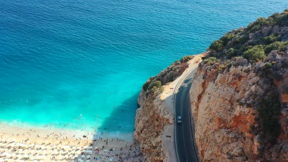 Aerial drone panning downward as cars drive alongside the Mediterranean coastal cliff road at Kaputa