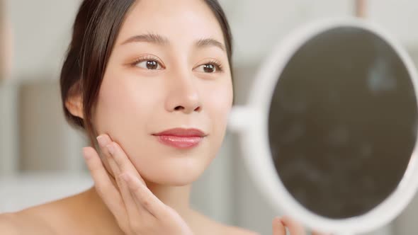 Happy attractive asian woman apply skincare cream on face