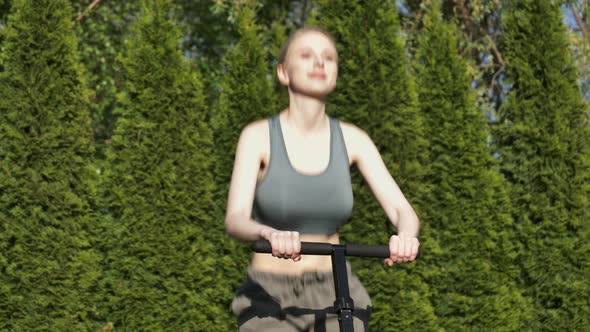 girl does Jumping fitness on trampoline in outdoor on green grass and trees on background