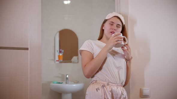 A Young Woman Drinking Coffee Standing in the Bathroom Doorway at the Morning